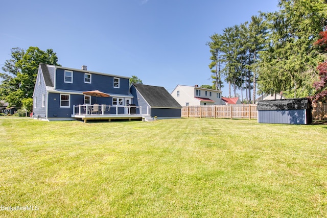 rear view of property with a storage unit, a deck, and a yard