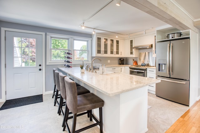 kitchen featuring appliances with stainless steel finishes, light stone counters, white cabinetry, a breakfast bar area, and extractor fan