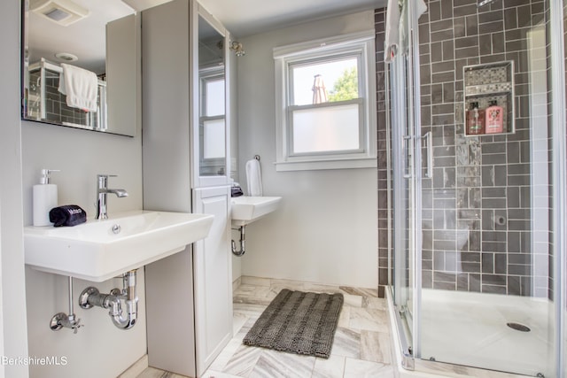 bathroom featuring a shower with shower door and sink