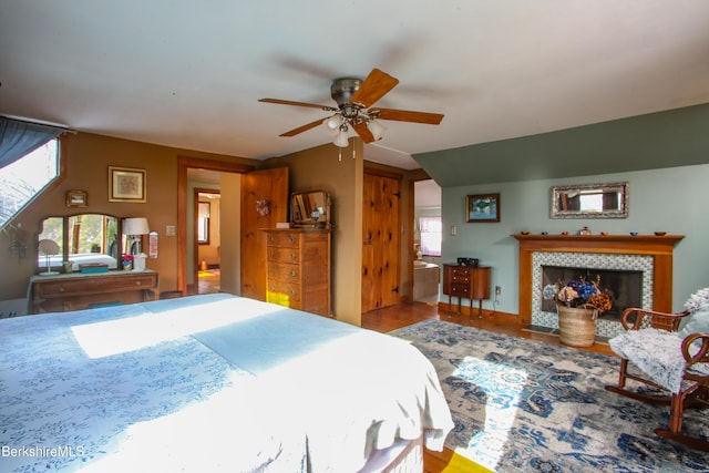 bedroom featuring hardwood / wood-style floors, a fireplace, ceiling fan, and ensuite bath