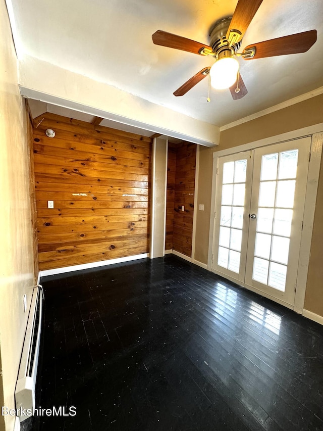 spare room with crown molding, a baseboard heating unit, wooden walls, wood-type flooring, and french doors