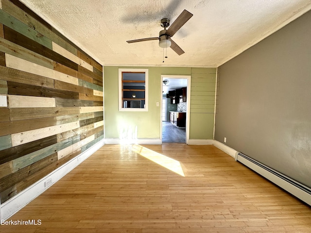 empty room with light hardwood / wood-style flooring, a textured ceiling, baseboard heating, wooden walls, and ceiling fan