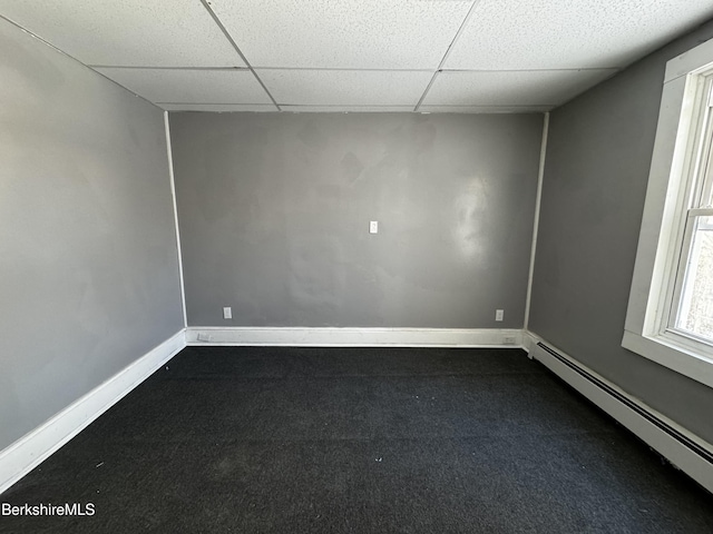 unfurnished room with dark colored carpet, a baseboard heating unit, and a drop ceiling