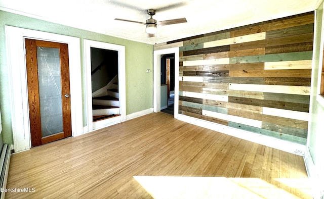 empty room with ceiling fan, a baseboard radiator, and wooden walls