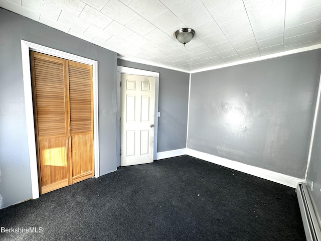 unfurnished bedroom featuring dark colored carpet, a closet, and a baseboard heating unit