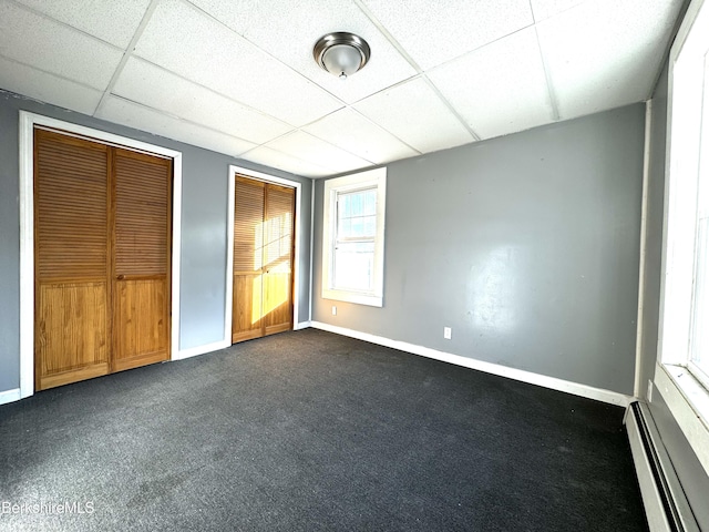 unfurnished bedroom featuring dark carpet, a paneled ceiling, multiple closets, and baseboard heating