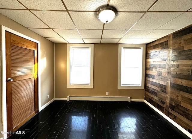 unfurnished room featuring a wealth of natural light, a baseboard radiator, and wooden walls