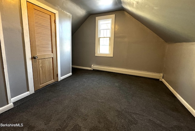 additional living space featuring dark colored carpet, lofted ceiling, and a baseboard heating unit