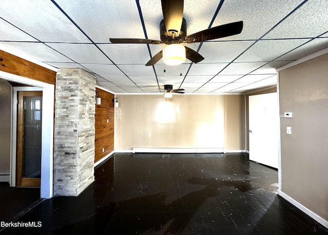 spare room with a drop ceiling, baseboard heating, and wood walls