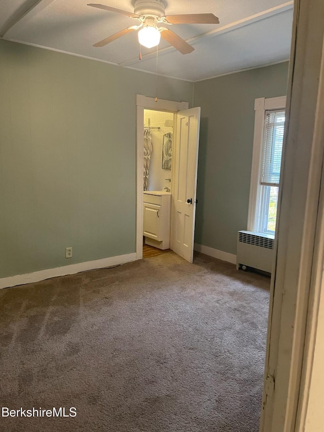 unfurnished bedroom with ensuite bath, ceiling fan, radiator heating unit, and light carpet