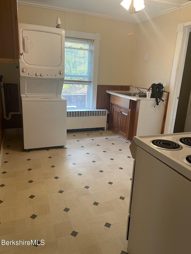 laundry room featuring radiator heating unit, ornamental molding, and stacked washer and clothes dryer