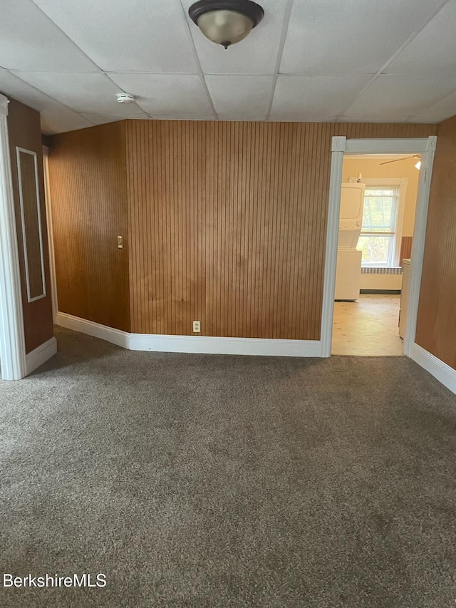 empty room featuring a paneled ceiling, carpet flooring, radiator heating unit, and wooden walls