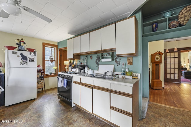 kitchen featuring a sink, light countertops, gas stove, white cabinets, and freestanding refrigerator