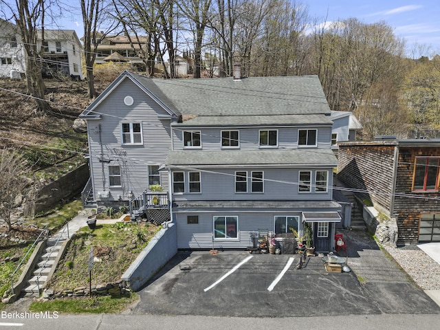 view of front facade featuring stairway, uncovered parking, and a shingled roof