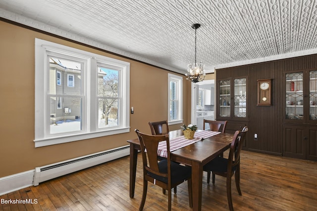 dining area with an inviting chandelier, ornamental molding, wood-type flooring, and a baseboard heating unit