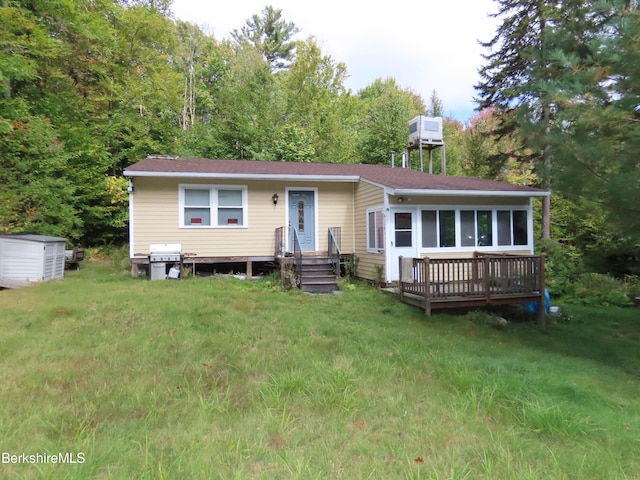 view of front facade featuring a wooden deck, a sunroom, a front yard, and central AC