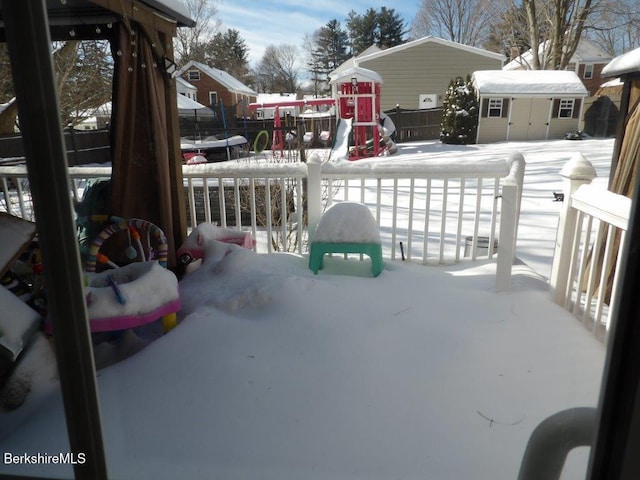 snow covered patio featuring a storage shed, a trampoline, an outbuilding, and fence