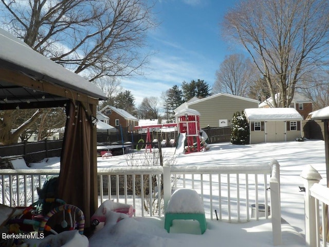 snow covered deck with a trampoline, an outdoor structure, fence, and a storage unit