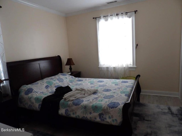 bedroom featuring ornamental molding, wood finished floors, visible vents, and baseboards