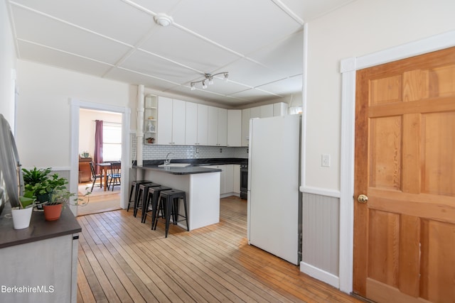 kitchen featuring light hardwood / wood-style flooring, range, white cabinetry, a kitchen breakfast bar, and white fridge