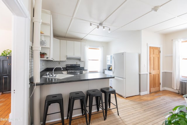 kitchen featuring a breakfast bar area, white cabinetry, white refrigerator, gas range, and kitchen peninsula