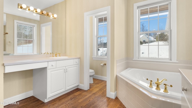 full bathroom with a garden tub, toilet, wood finished floors, vanity, and baseboards