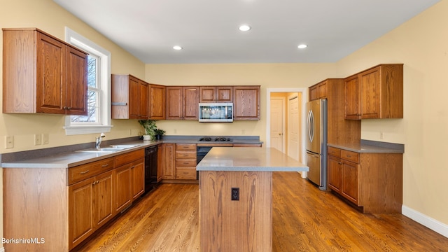 kitchen with a center island, brown cabinetry, a sink, wood finished floors, and black appliances