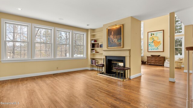 living room with wood finished floors, a glass covered fireplace, built in shelves, and baseboards