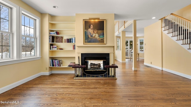 sitting room featuring a multi sided fireplace, wood finished floors, baseboards, stairs, and built in features