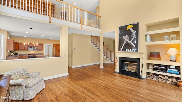 living room with an inviting chandelier, a fireplace with flush hearth, wood finished floors, baseboards, and stairs