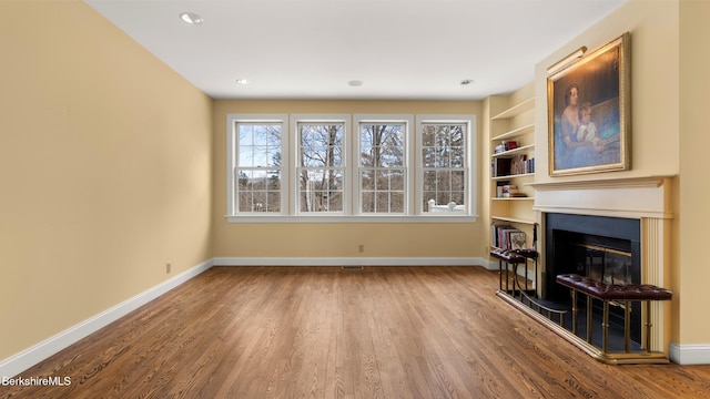 unfurnished living room featuring baseboards, wood finished floors, and a glass covered fireplace