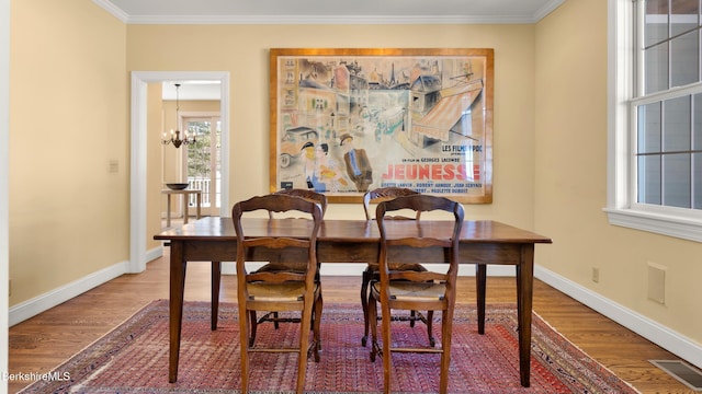 dining area with wood finished floors, visible vents, baseboards, ornamental molding, and an inviting chandelier