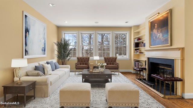 living room with baseboards, a glass covered fireplace, wood finished floors, built in shelves, and recessed lighting