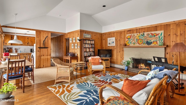 living area with light wood finished floors, baseboard heating, a brick fireplace, and wooden walls