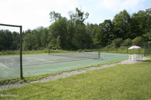 view of tennis court with a yard and fence