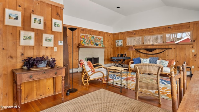 living area with lofted ceiling, wood finished floors, wood walls, a fireplace, and a baseboard heating unit