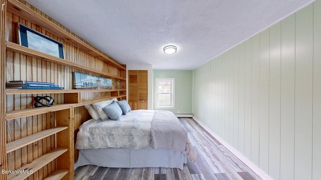 208 Columbia St, Adams, MA 01220 - bedroom featuring wooden walls, a baseboard radiator, wood finished floors, and a textured ceiling