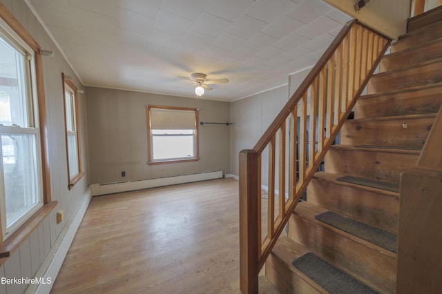 stairs with wood-type flooring, ornamental molding, ceiling fan, and baseboard heating