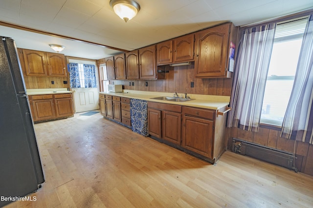 kitchen with sink, light hardwood / wood-style flooring, baseboard heating, wooden walls, and black fridge