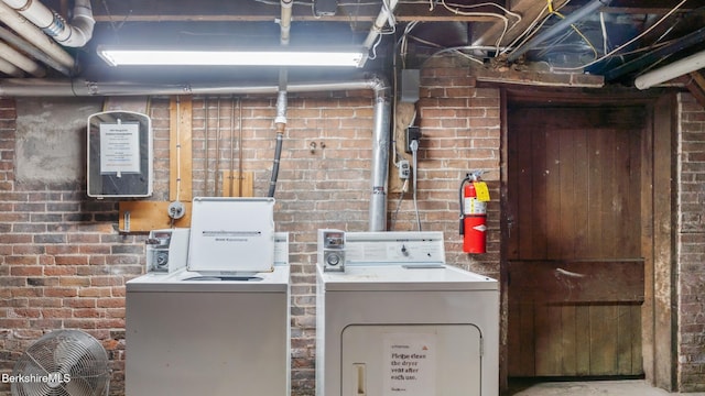 clothes washing area with laundry area, separate washer and dryer, and brick wall