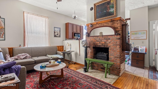 living room featuring light wood-style floors, a fireplace, a ceiling fan, and a textured ceiling