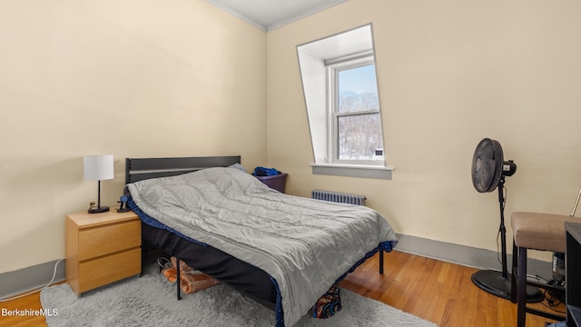 bedroom with radiator, baseboards, ornamental molding, and wood finished floors