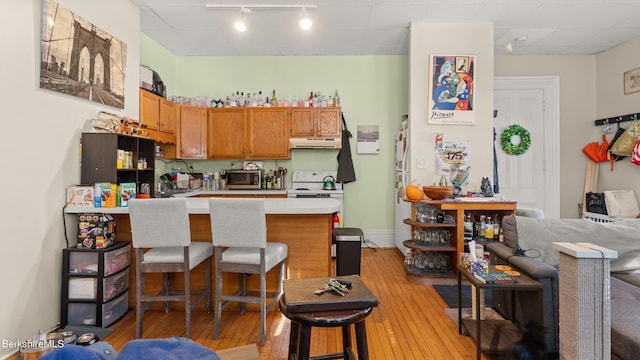 kitchen with light wood-style flooring, a breakfast bar area, a peninsula, light countertops, and under cabinet range hood