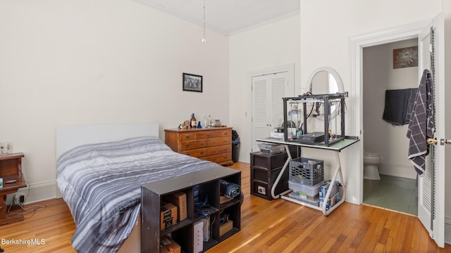 bedroom with ensuite bathroom, wood finished floors, baseboards, a closet, and crown molding