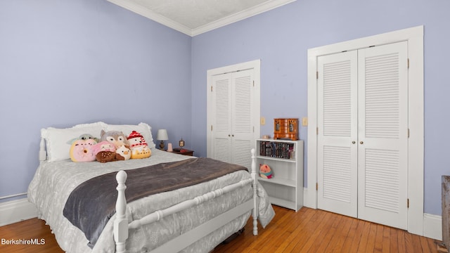 bedroom with multiple closets, ornamental molding, and hardwood / wood-style floors