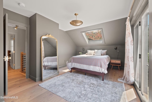 bedroom with light wood-style floors, baseboards, and vaulted ceiling with skylight