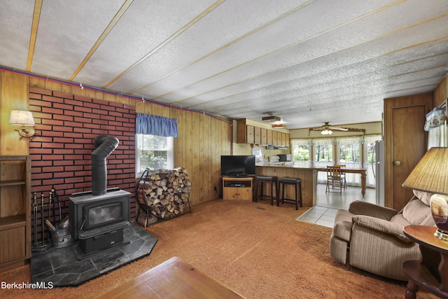 159 Black Brook Rd, Savoy, MA 01256 - living room featuring a wood stove, wooden walls, a textured ceiling, light carpet, and ceiling fan