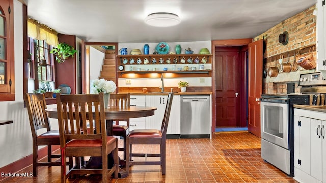 bar featuring white cabinets, appliances with stainless steel finishes, brick wall, and sink