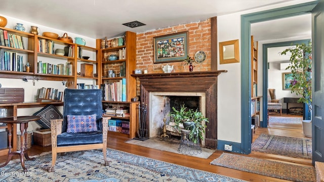 sitting room featuring wood-type flooring and a brick fireplace