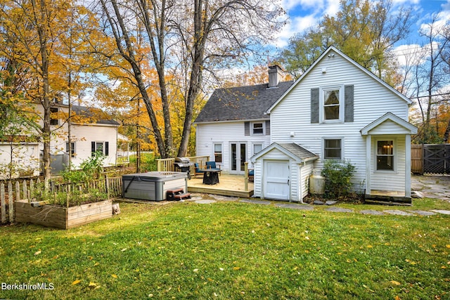 rear view of house with a hot tub, a deck, and a lawn